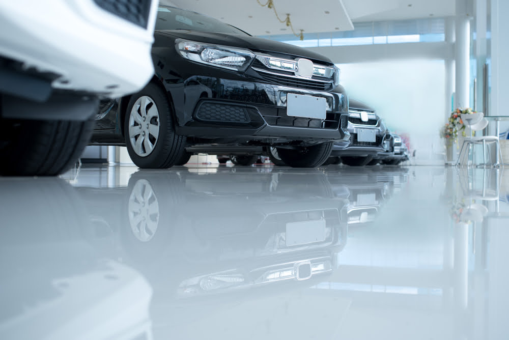 A row of luxury cars lined up in a car dealership showroom for display. The cars in this garage are parked on a white epoxy floor. Epoxy Flooring is the perfect canvas to show off expensive cars in a garage or a showroom.